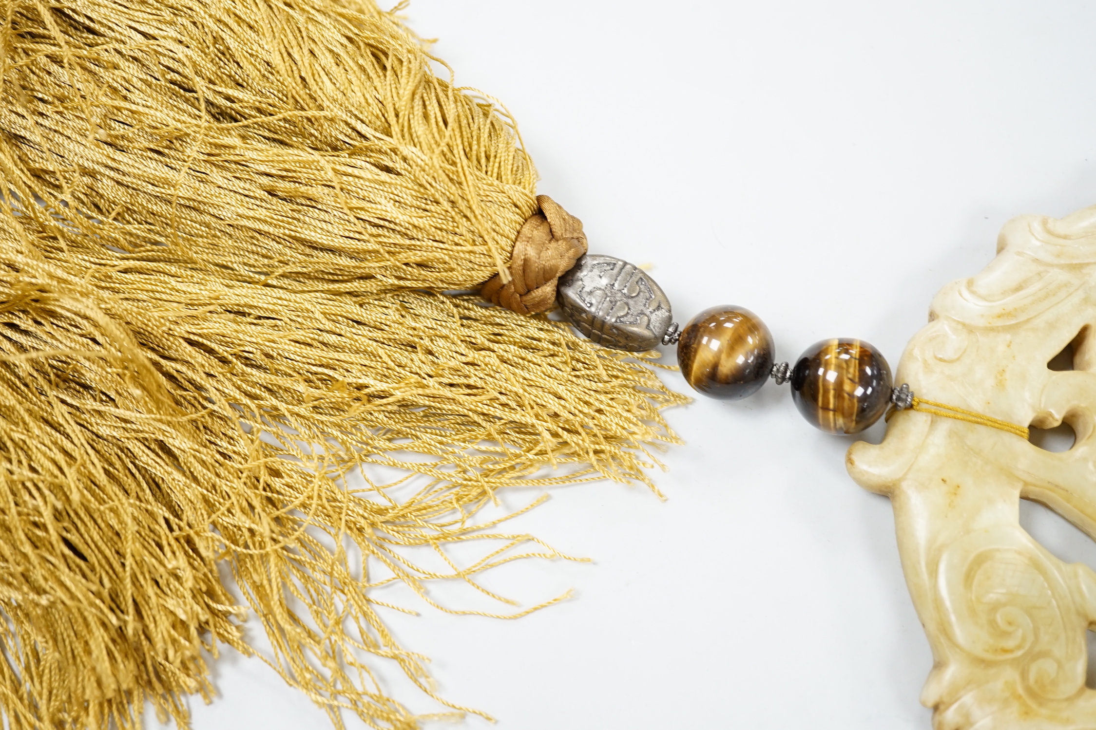 A large Chinese bowenite jade disc, threaded with tiger's eye beads and long silk tassel, 90cm long